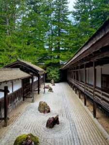 A tranquil Japanese Zen garden surrounded by traditional wooden architecture and lush greenery.